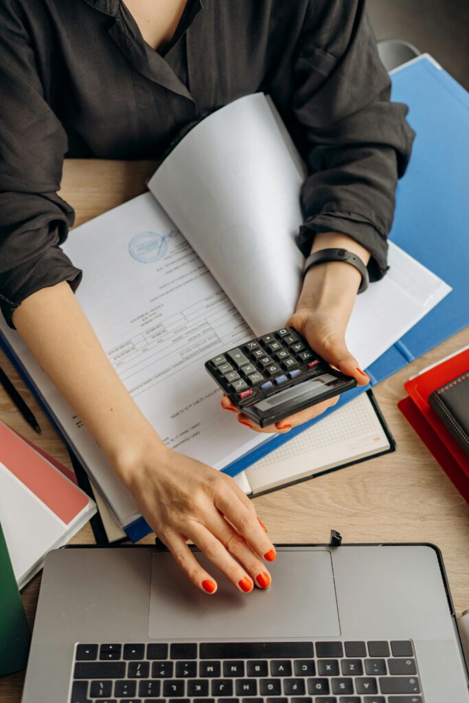 pexels-photo-8296981-8296981 A business professional uses a calculator among documents and laptop on a desk for financial tasks.